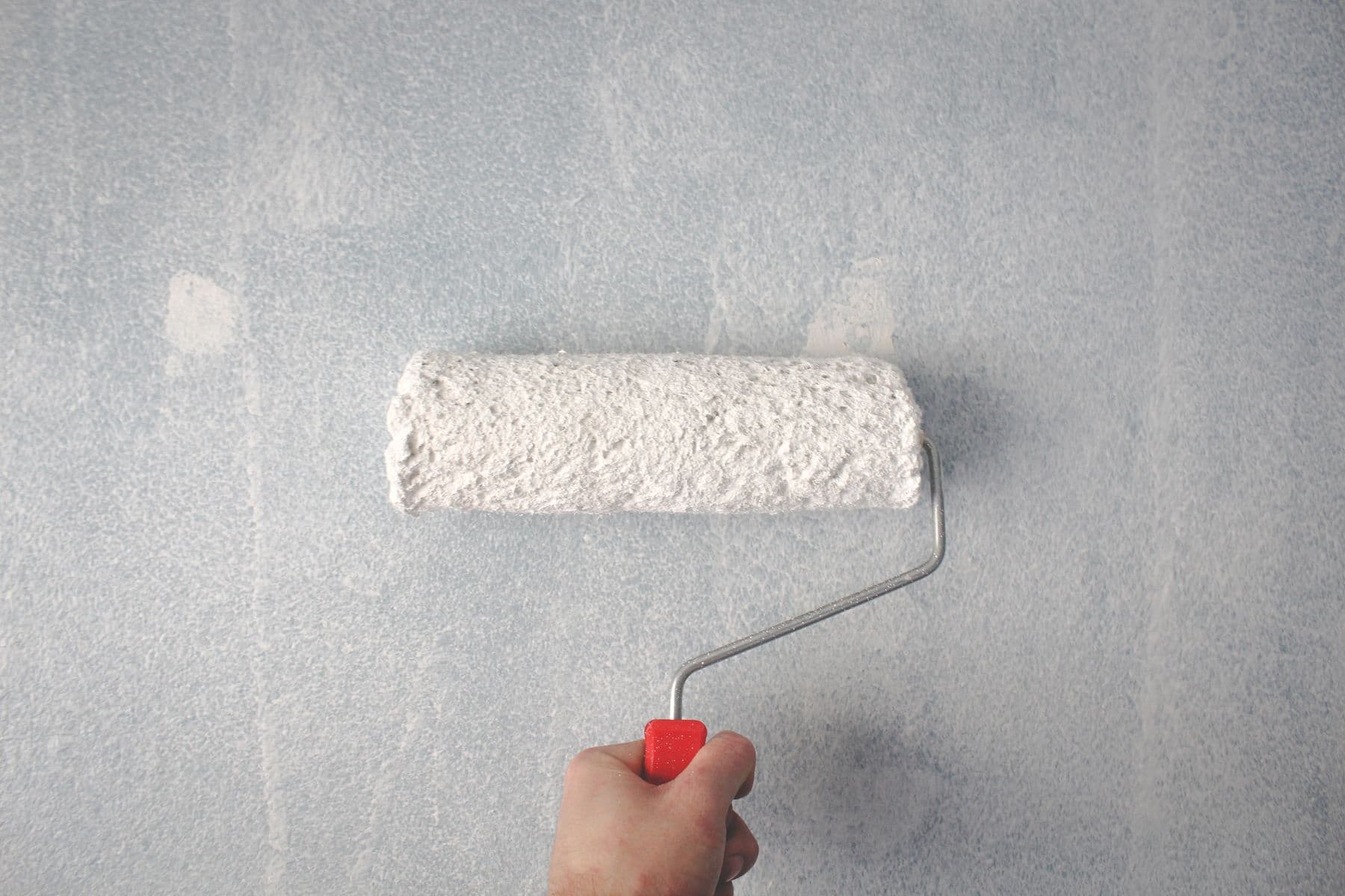 A hand rolling white paint onto a gray wall.