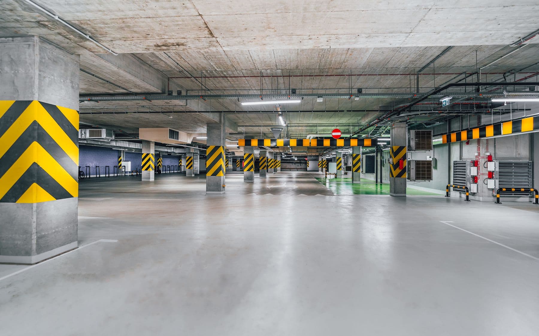 An empty parking garage with a gray coated floor and columns striped in yellow and black.