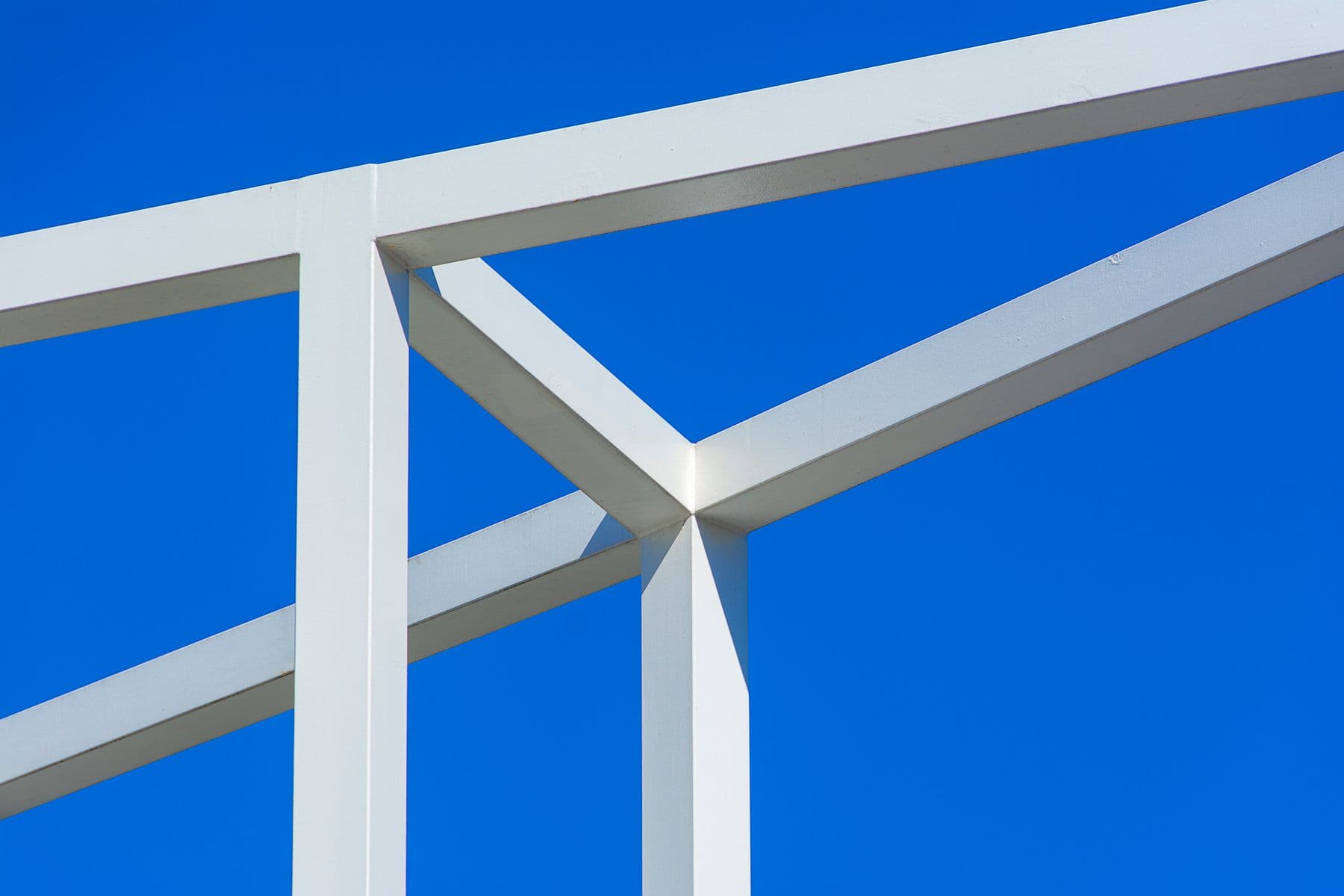 White painted steel members meeting at a joint against a blue sky.